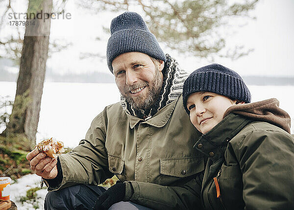 Lächelnder reifer Mann isst Hotdog mit Sohn im Winter