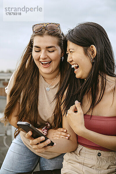 Junge Frauen lachen beim Teilen eines Smartphones