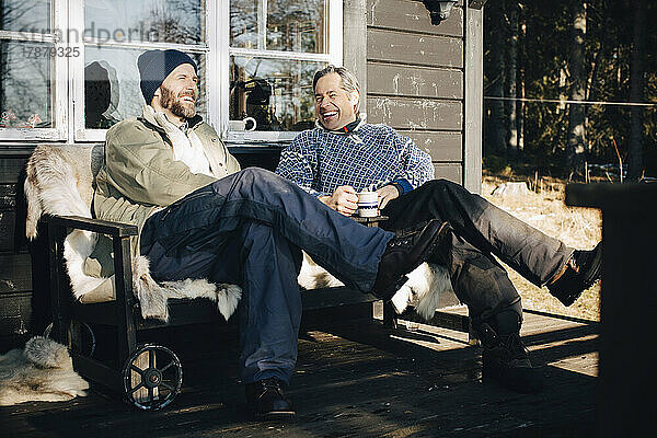 Fröhliche reife Männer unterhalten sich beim gemeinsamen Kaffee auf der Veranda im Winter