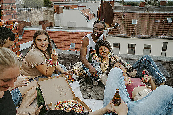 Glückliche männliche und weibliche Freunde mit Pizza  die eine Party auf dem Dach genießen