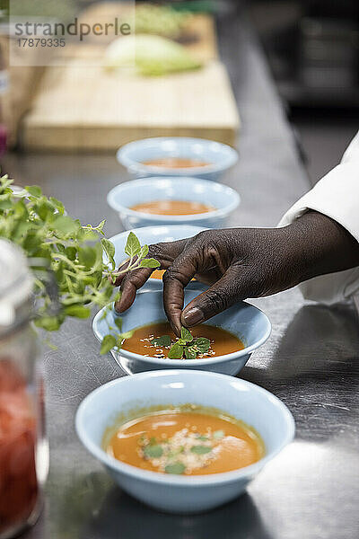 Abgeschnittene Hand einer Frau  die eine Suppe auf der Küchentheke eines Restaurants garniert