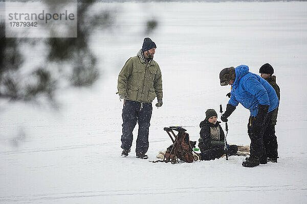 Ältere Männer beim Eisfischen mit ihren Söhnen auf einem zugefrorenen See im Urlaub