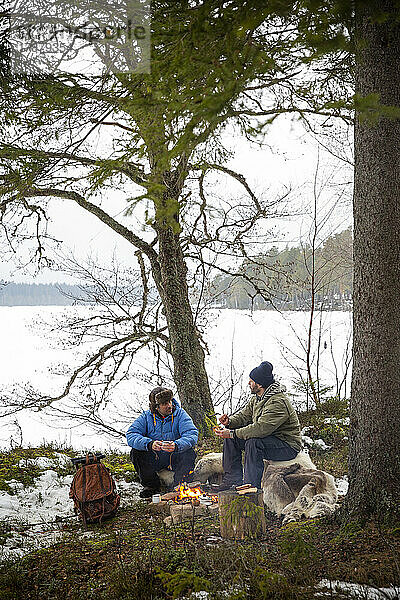 Männliche Freunde  die sich am Lagerfeuer unterhalten  während sie im Winter sitzen