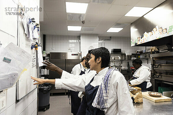 Kleinunternehmer planen  während sie auf ein Whiteboard in einer Restaurantküche zeigen