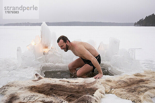 Fröhlicher reifer Mann genießt Eisbad auf zugefrorenem See im Urlaub