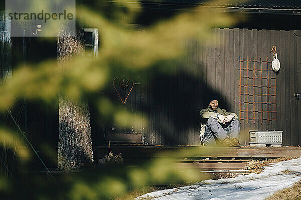 Älterer Mann sitzt auf der Veranda an einem sonnigen Tag im Winter