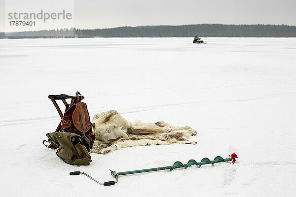 Rucksack mit Tierfell und Eisbohrer auf Schnee im Winter