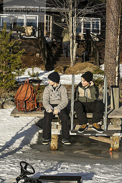 Jungen in voller Länge auf dem Steg sitzend an einem sonnigen Tag
