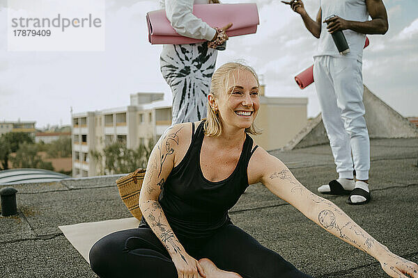 Glückliche Frau  die Yoga praktiziert  während Freunde auf dem Dach stehend miteinander reden
