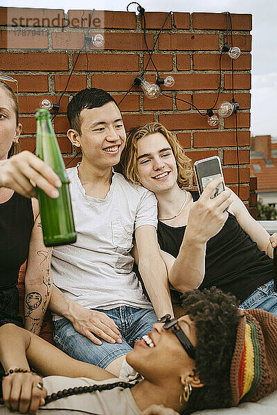 Lächelnde Männer teilen sich das Handy mit ihren Freundinnen auf dem Dach