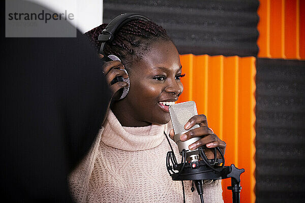Lächelnde Sängerin beim Einstellen der Kopfhörer während der Aufnahme eines Songs im Studio