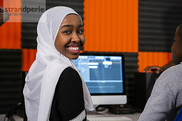 Porträt eines lächelnden Mädchens mit Hidschab  das im Aufnahmestudio sitzt
