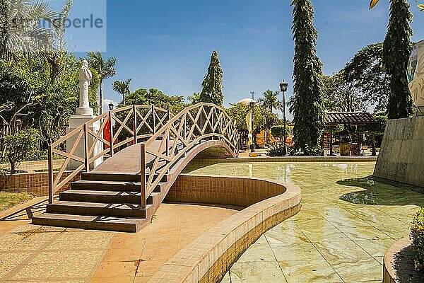 Blick auf einen ruhigen Park mit einer kleinen Holzbrücke über einen Wasserbrunnen. Nagarote Zentralpark. Bild eines schönen und entspannten Parks mit einem von Bäumen umgebenen Wasserbrunnen. Traditioneller Park von Nagarote  Nicaragua  Mittelamerika