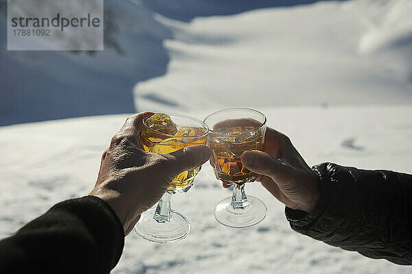 Nahaufnahme der POV-Hände von Freunden  die im Schnee Apres-Ski-Cocktails anstoßen