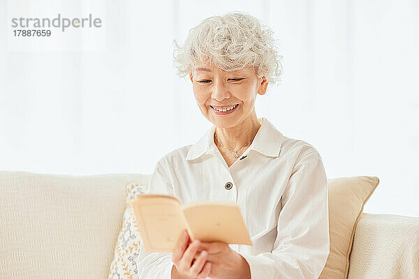 Japanische Seniorin liest ein Buch auf dem Sofa