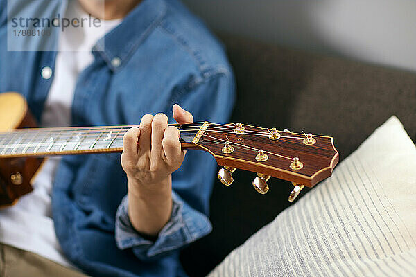 Japanischer Mann spielt Gitarre auf dem Sofa