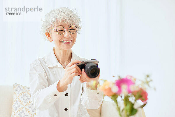 Japanische Seniorin fotografiert Blumen auf dem Sofa