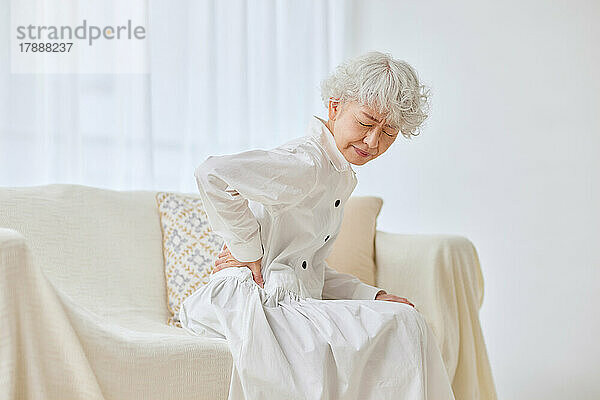 Japanischer Senior mit Schmerzen auf dem Sofa