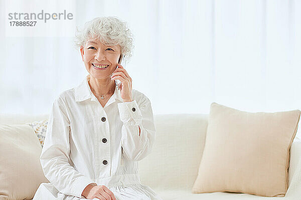 Japanische Seniorin benutzt Smartphone auf dem Sofa
