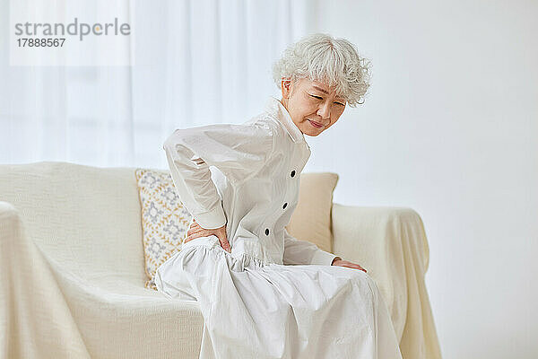 Japanischer Senior mit Schmerzen auf dem Sofa