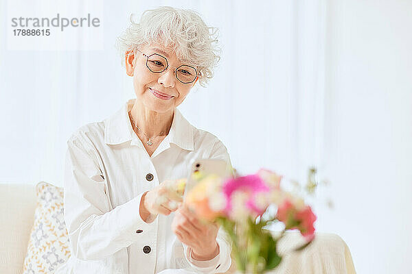 Japanische Seniorin  die auf dem Sofa Blumen fotografiert