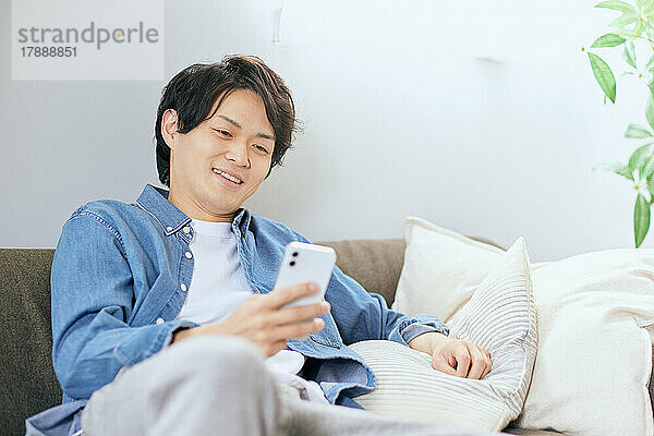 Japaner benutzt Smartphone auf dem Sofa