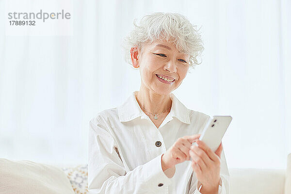 Japanische Seniorin benutzt Smartphone auf dem Sofa