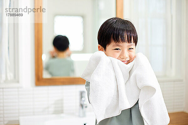 Japanisches Kind wischt sich zu Hause das Gesicht mit einem Handtuch ab
