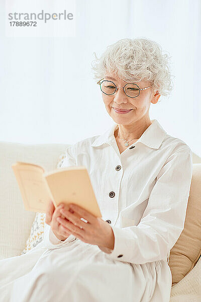 Japanische ältere Frau liest ein Buch auf dem Sofa