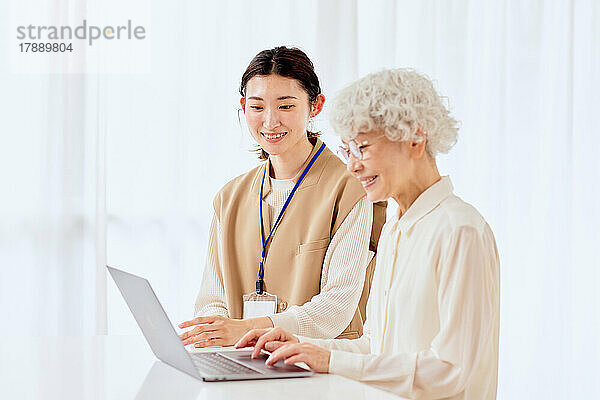 Eine japanische Seniorin lernt  zu Hause einen Laptop zu benutzen