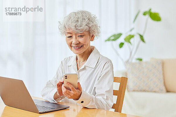 Japanische Seniorin benutzt Laptop und Smartphone zu Hause