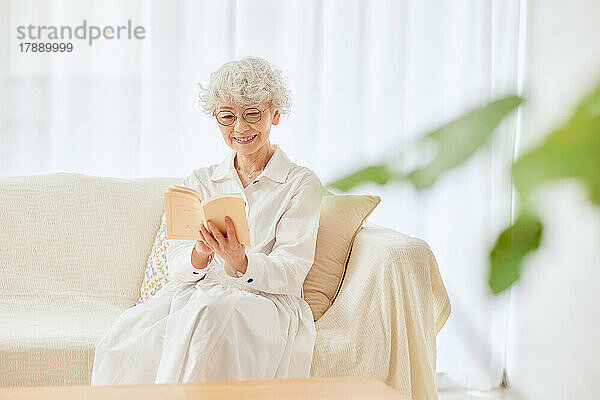 Japanische Seniorin liest ein Buch auf dem Sofa