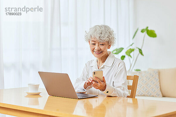 Japanische Seniorin nutzt Laptop und Smartphone zu Hause