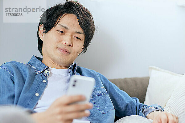 Japaner benutzt Smartphone auf dem Sofa