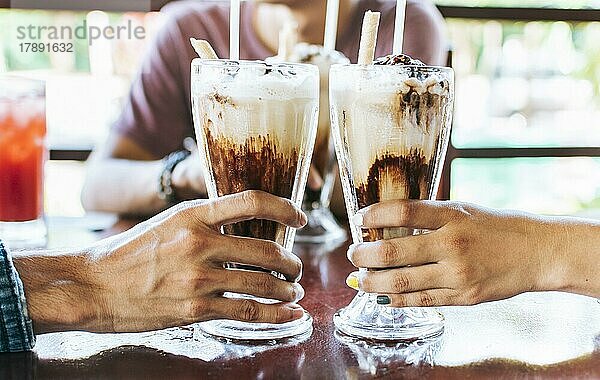 Mann und Frau Hand Toasting und hält zwei Milchshake. Zwei Hände stoßen mit Milchshake in einem Café an  Nahaufnahme von zwei Händen  die mit Eiskaffee in einem Café anstoßen