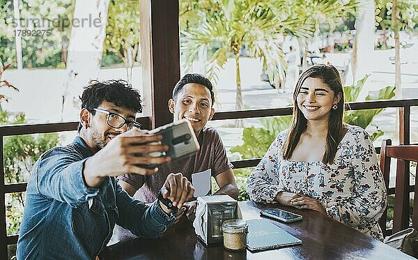 Junge Freunde machen ein Selfie in einem Café. Drei glückliche Menschen in einem Café  die ein Selfie machen. Frontansicht von Teenager-Freunden  die ein Selfie machen und Spaß in einem Cafe-Restaurant haben