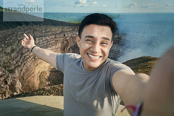 Ein Tourist  der ein Selfie vor einem Aussichtspunkt macht. Glücklicher Tourist  der ein Urlaubs-Selfie macht. Hombre aventurero haciéndose un selfie en un mirador. Primer plano de la persona que toma un selfie de aventura. Volcán Masaya  Nicaragua  Mittelamerika