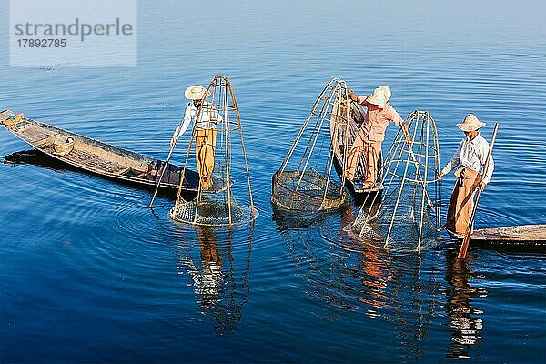 Myanmar Reiseattraktion Wahrzeichen  drei traditionelle birmanische Fischer balancieren mit Fischernetz am Inle-See in Myanmar berühmt für ihre unverwechselbaren einbeinigen Ruderstil