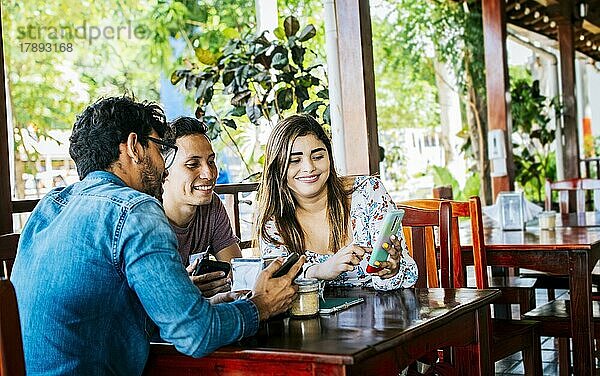 Junge Freunde in einem Café mit ihren Handys  die sich amüsieren. Drei Menschen in einem Café mit Handys  die sich amüsieren. Drei Teenager-Freunde mit ihren Handys in einem Café
