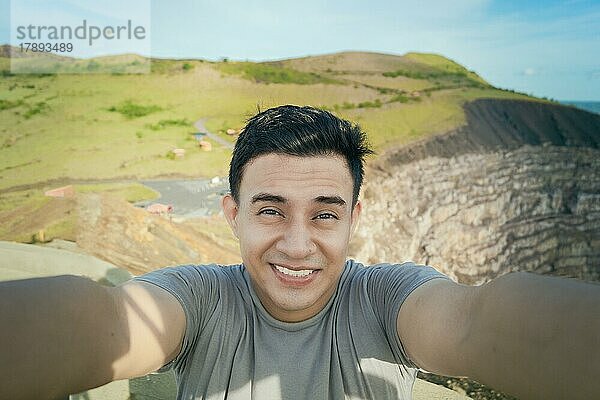 Abenteuerlustiger Mann macht ein Selfie an einem Aussichtspunkt. Nahaufnahme einer Person  die ein abenteuerliches Selfie macht  Tourist  der ein Selfie an einem Aussichtspunkt macht. Gutaussehender Tourist macht ein Selfie im Urlaub. Volcán Masaya  Nicaragua  Mittelamerika