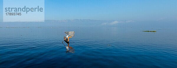 Panorama eines traditionellen birmanischen Fischers  der mit einem Fischernetz auf dem Inle-See balanciert  Myanmar  das für seinen unverwechselbaren einbeinigen Ruderstil bekannt ist  Asien