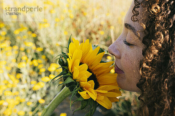 Junge Frau riecht gelbe Sonnenblume im Park