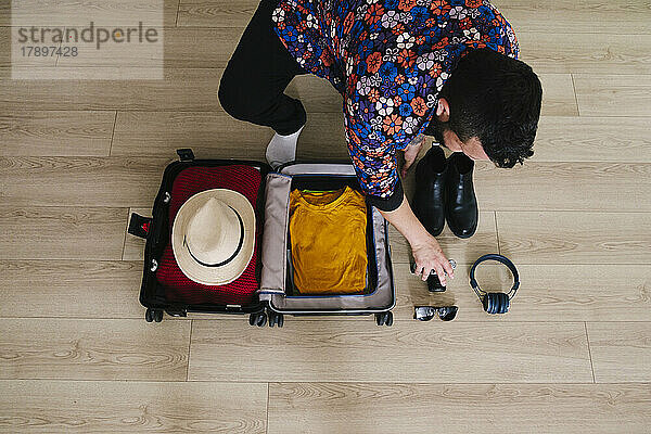 Reifer Mann hebt Kamera mit Koffer auf dem Boden zu Hause auf