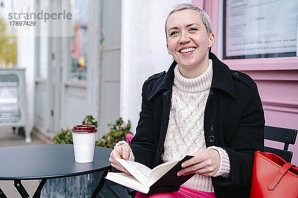 Glückliche Frau liest Buch im Straßencafé