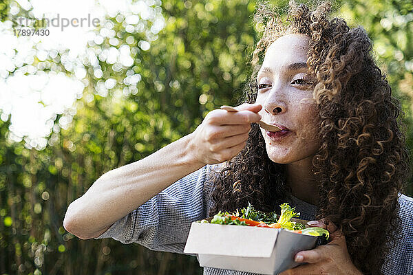 Junge Frau isst an einem sonnigen Tag Gemüsesalat im Park