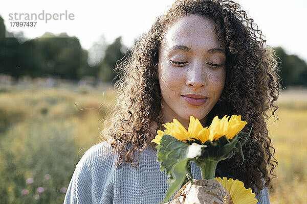 Frau mit lockigem Haar blickt auf Sonnenblume