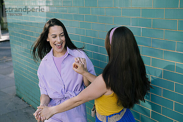Happy friends dancing with each other near brick wall