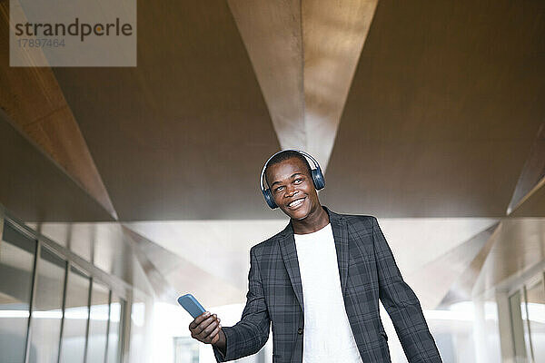 Glücklicher junger Mann mit Mobiltelefon  der über drahtlose Kopfhörer Musik hört