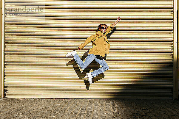 Happy young woman with hand raised jumping in front of shutter