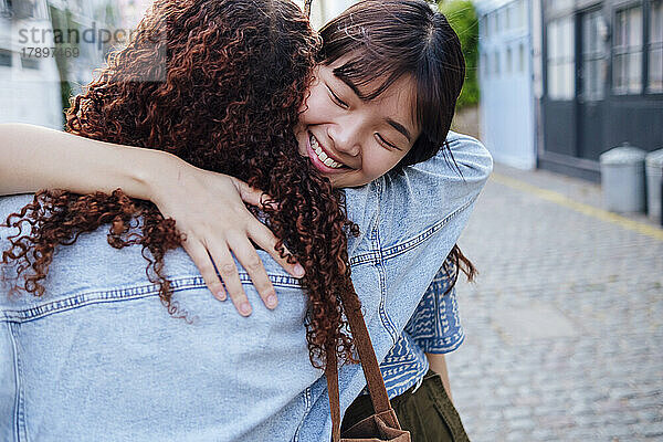 Lächelnde junge Frau umarmt Freund auf der Straße